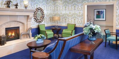 Sitting area with blue carpet, patterned wallpaper, bright furniture, and dark wood.