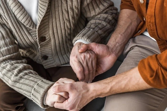 Father with dementia holds son’s hands