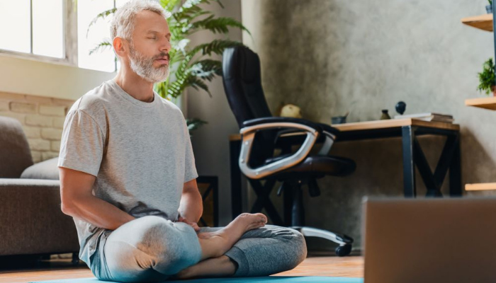 Senior man meditating seated on office floor.