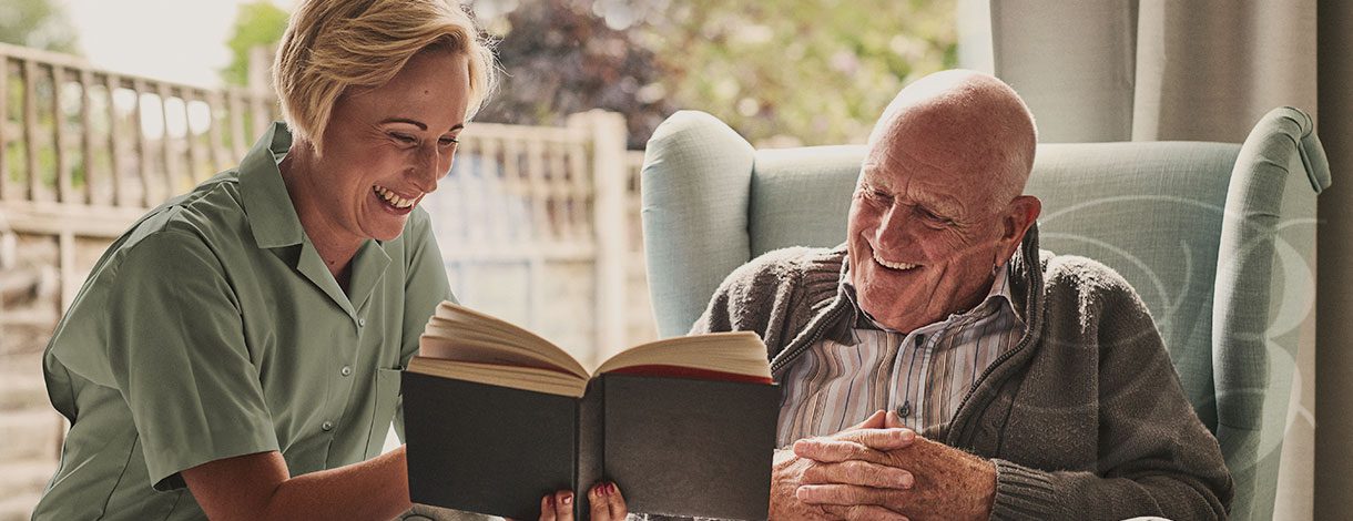 Senior citizen and caregiver reading a book and smiling