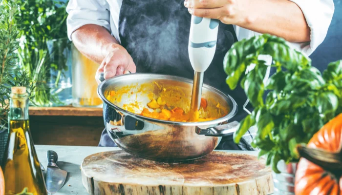 Chef using an immersion blender in metal bowl to make a dish for seniors