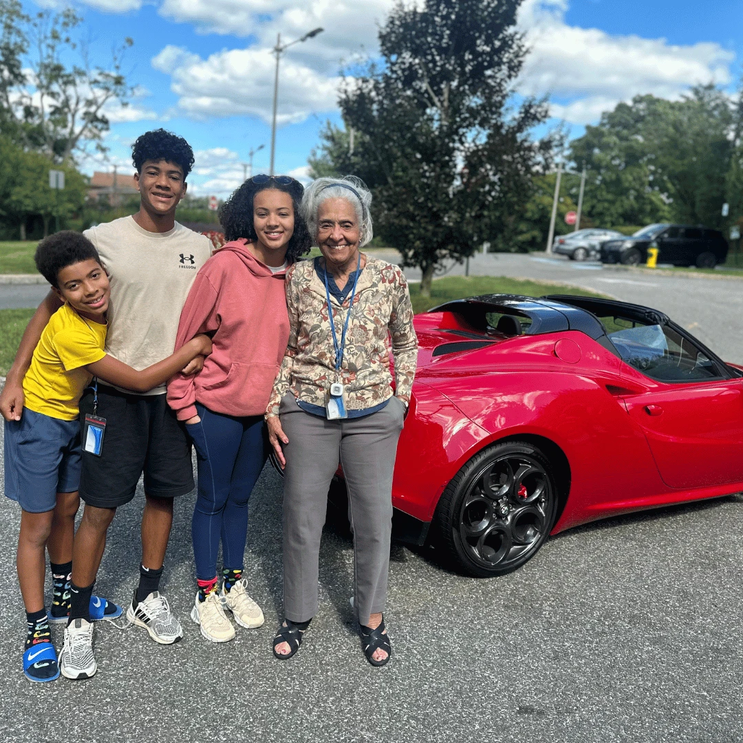White Plains resident poses with her grandchildren in front of a flashy, fast car.
