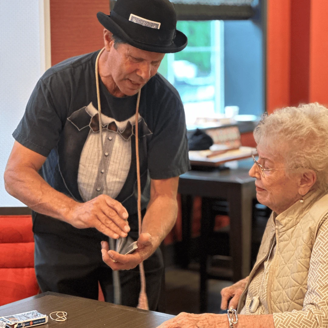 A magician does close-up sleight-of-hand to entertain a grandparent at The Bristal at White Plains.