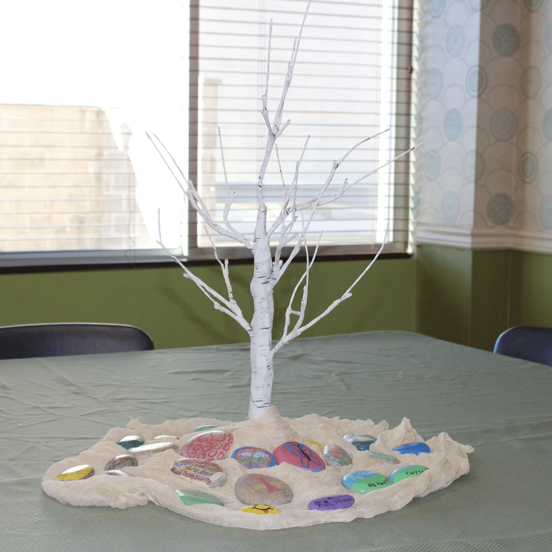 The inspiring kindness rocks staged around a small tree for photos before being placed outside.