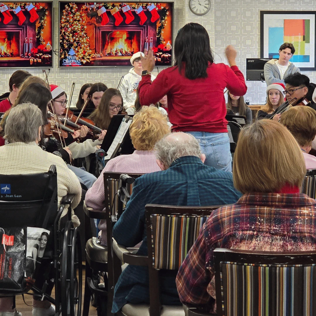 conductor stands before high school musicians leading musical performance for senior residents