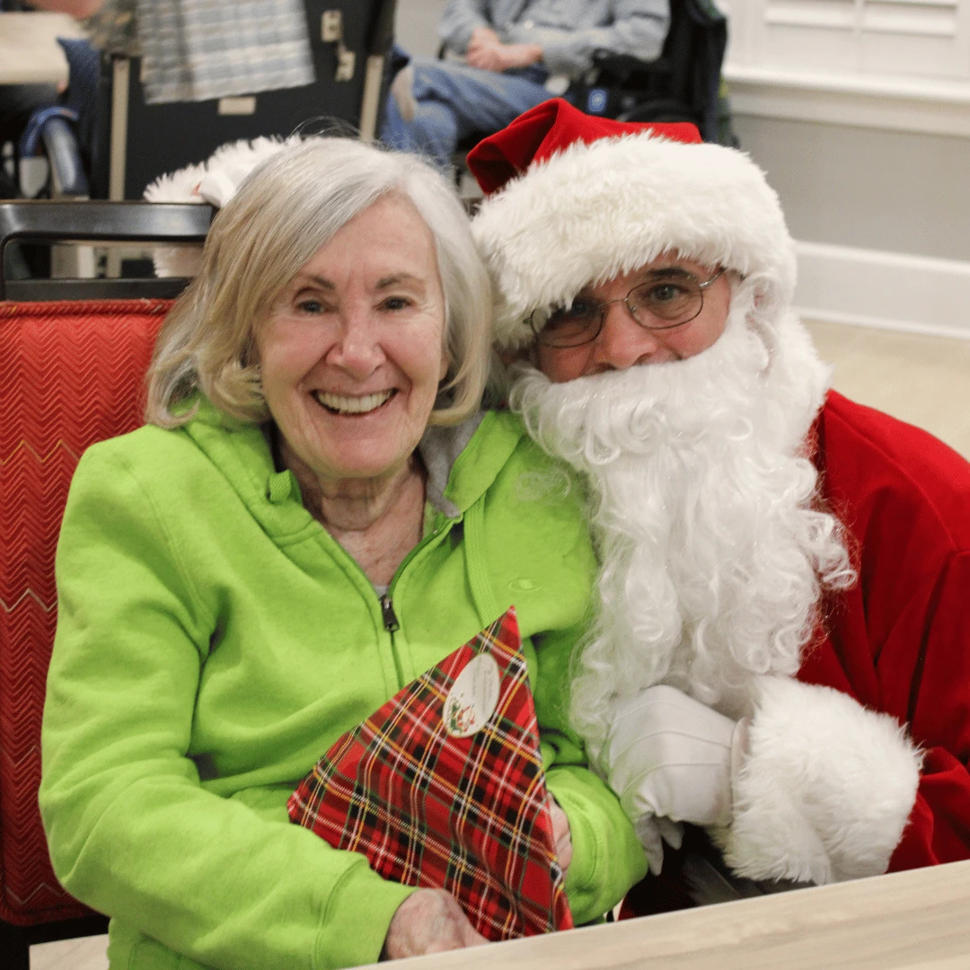 Resident of The Bristal at Mount Sinai smiles with Santa and holds a gift
