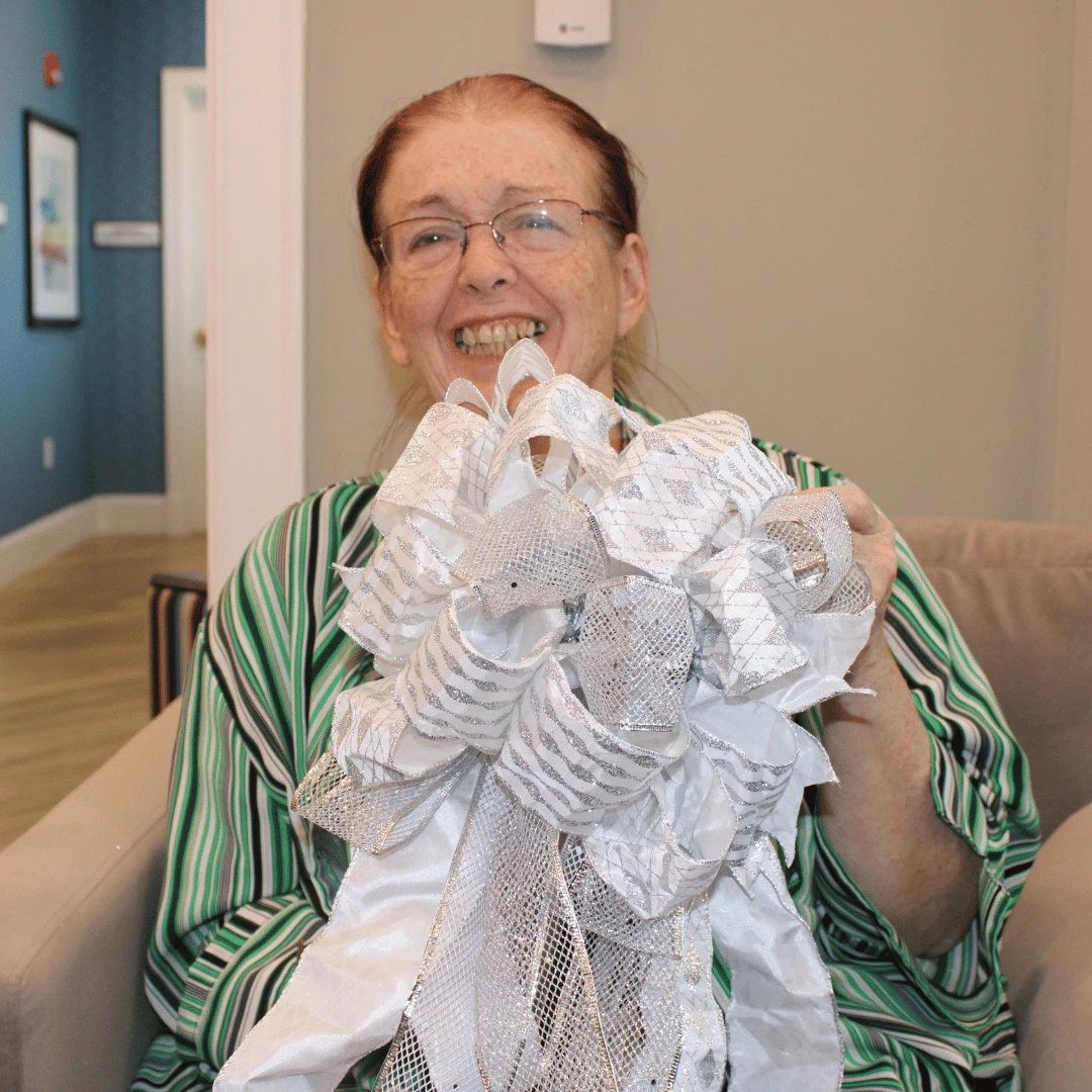 Resident poses with a large white bow to trim the tree at Somerset