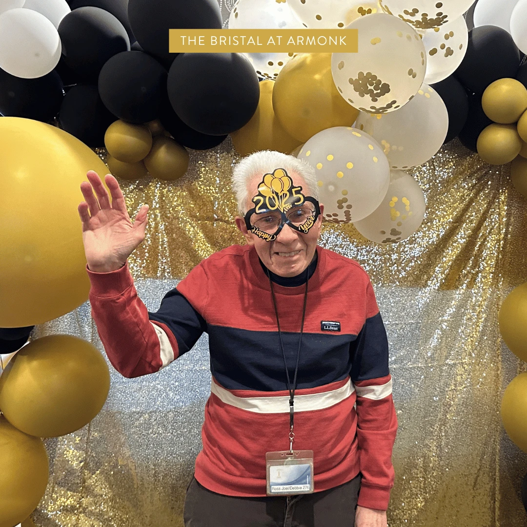 Resident poses for a photo in front of the balloon wall wearing 2025 festive glasses