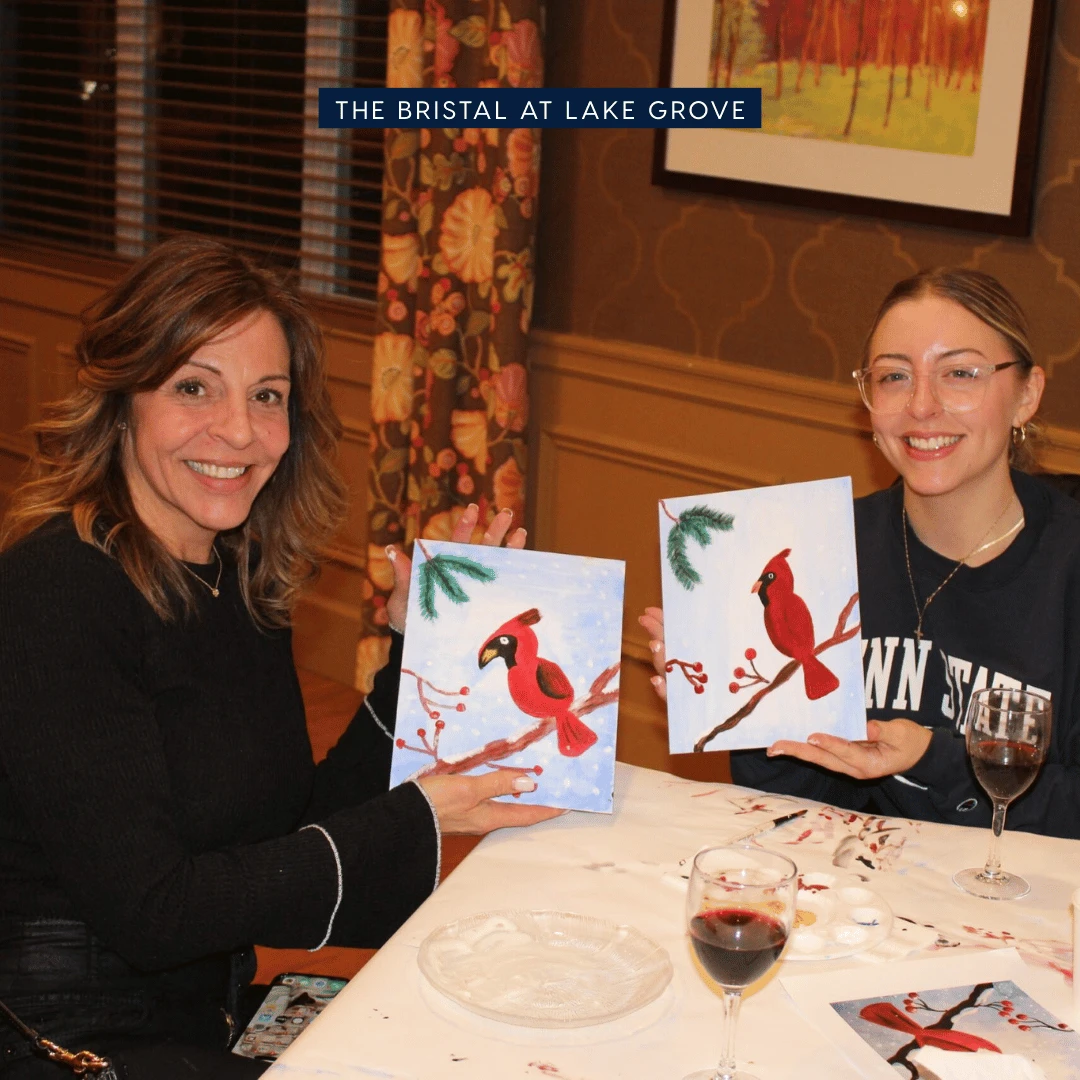 Two ladies from The Bristal at Lake Grove show off their cardinal paintings at the Paint and Sip for National Caregivers Day