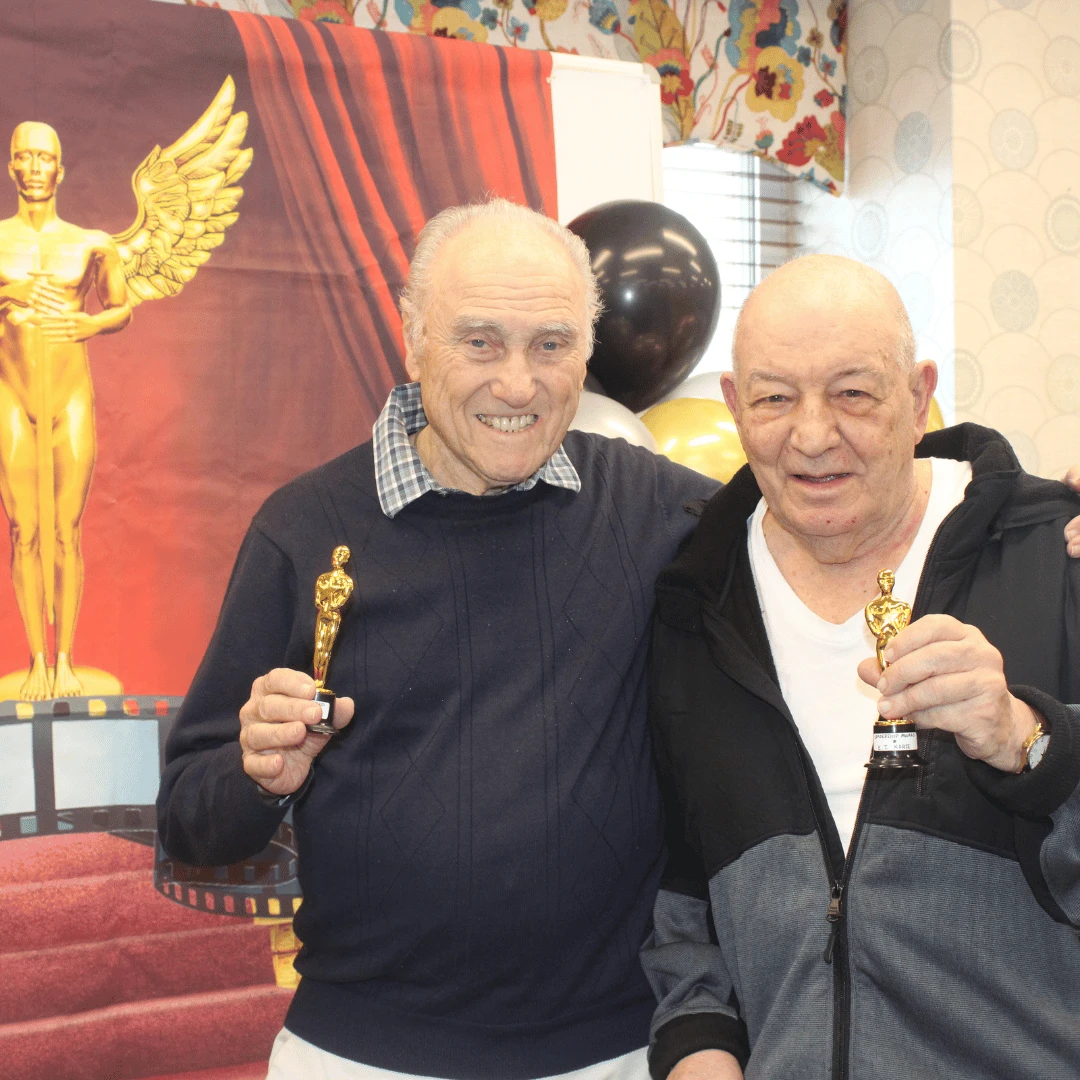 Two men pose holding their awards in front of an Academy-inspired backdrop