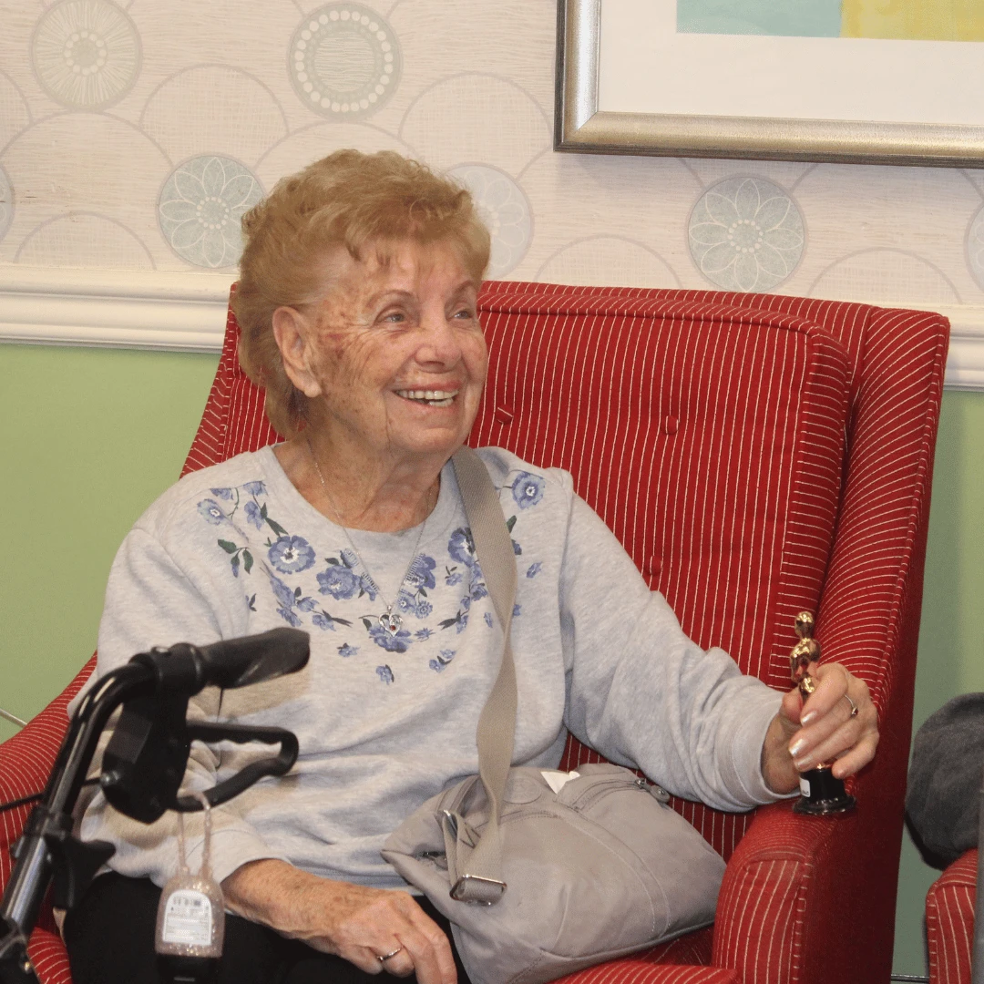 A senior woman sits smiling while holding her award