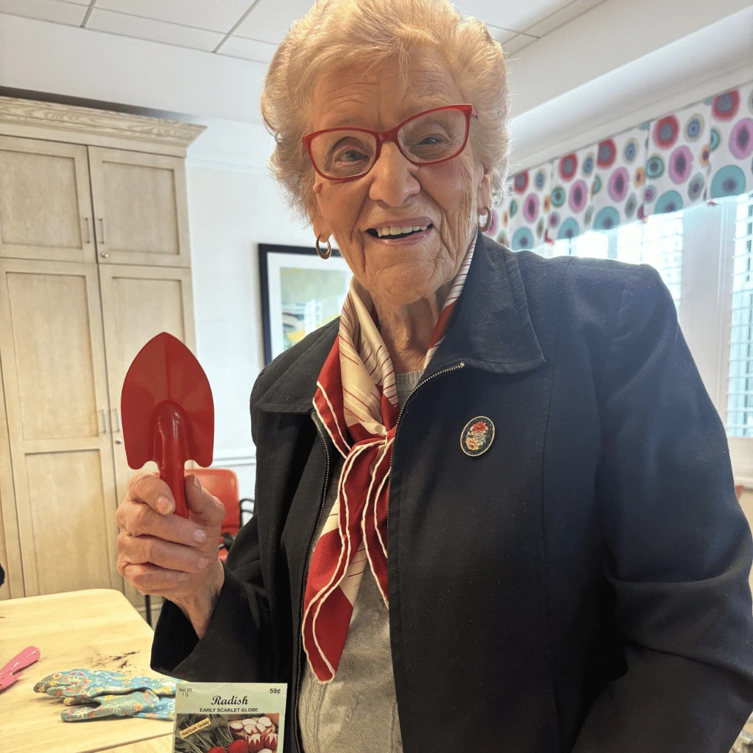 Resident of The Bristal at North Woodmere holds a spade and plants radishes