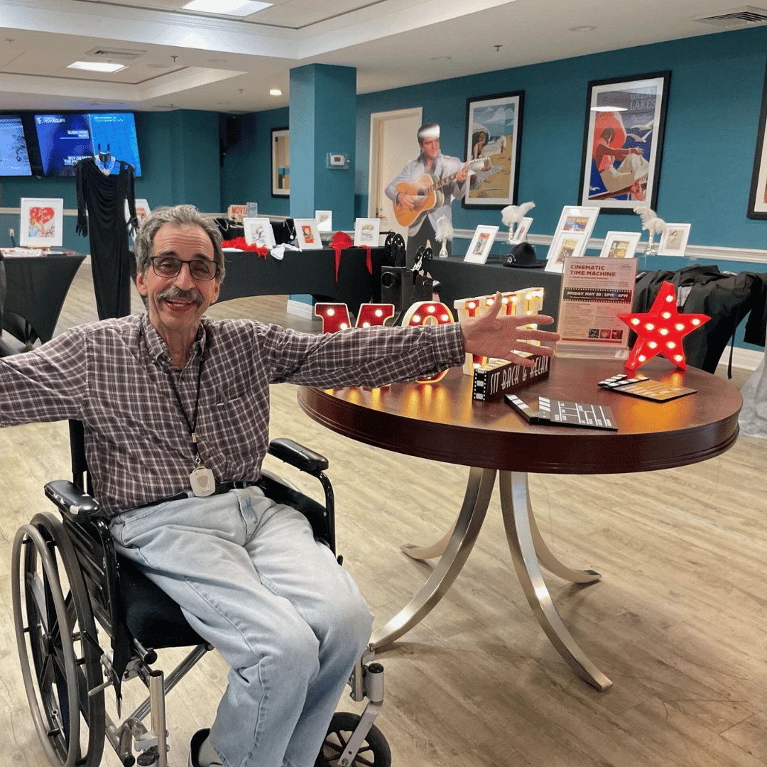 Senior Westbury resident smiles and poses in front of multiple film exhibits at the event at The Bristal