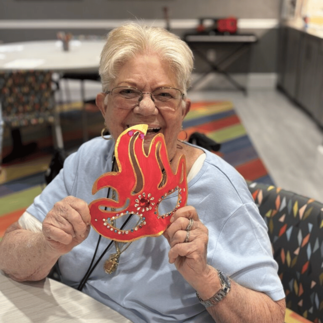 Resident from THe Bristal at Bethpage holds up a handmade Venetian mask from her journey around the world