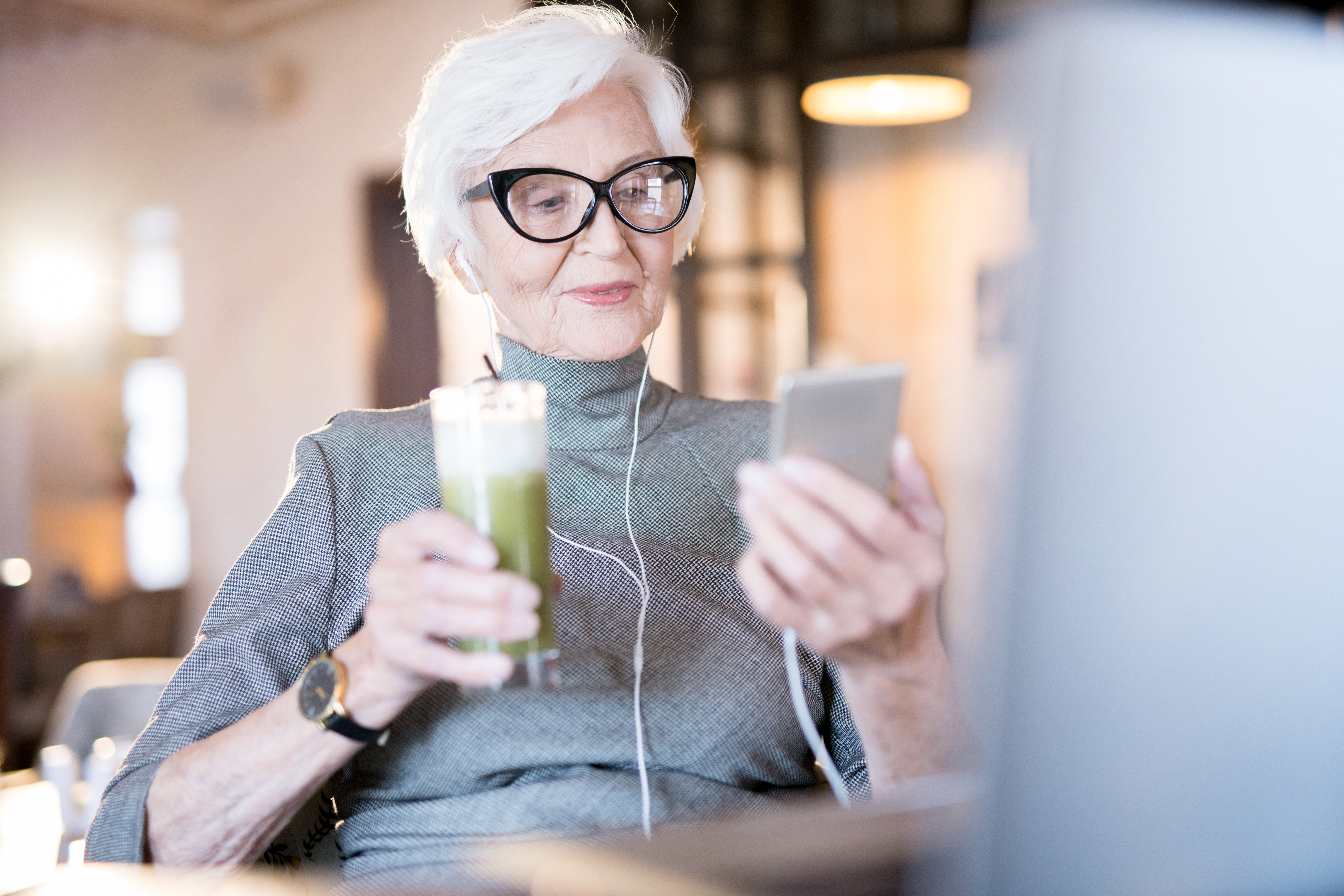 Senior woman resident of The Bristal with mobile phone relaxing with a beverage in the bistro