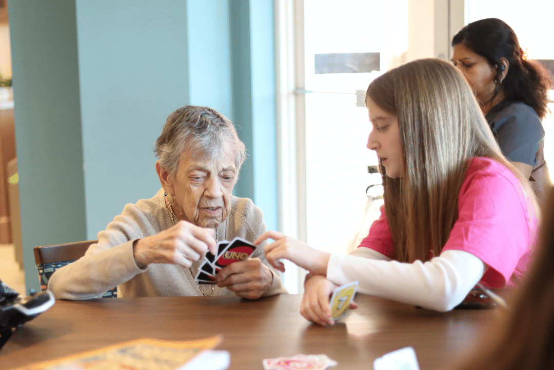 A resident of The Bristal at East Meadow plays card games with a volunteer from GlamourGals