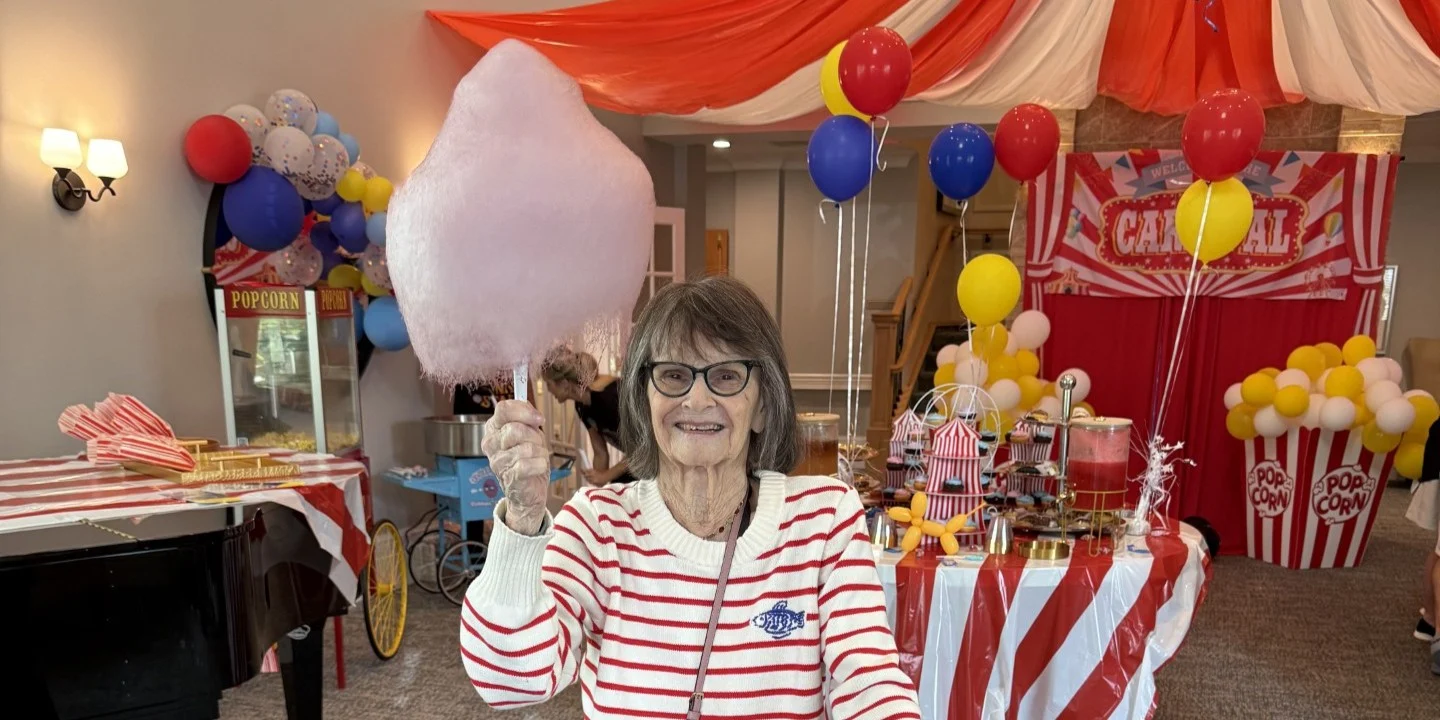 Grandparents Day at The Bristal at Sayville - Resident displays cotton candy in front of carnival themed decor